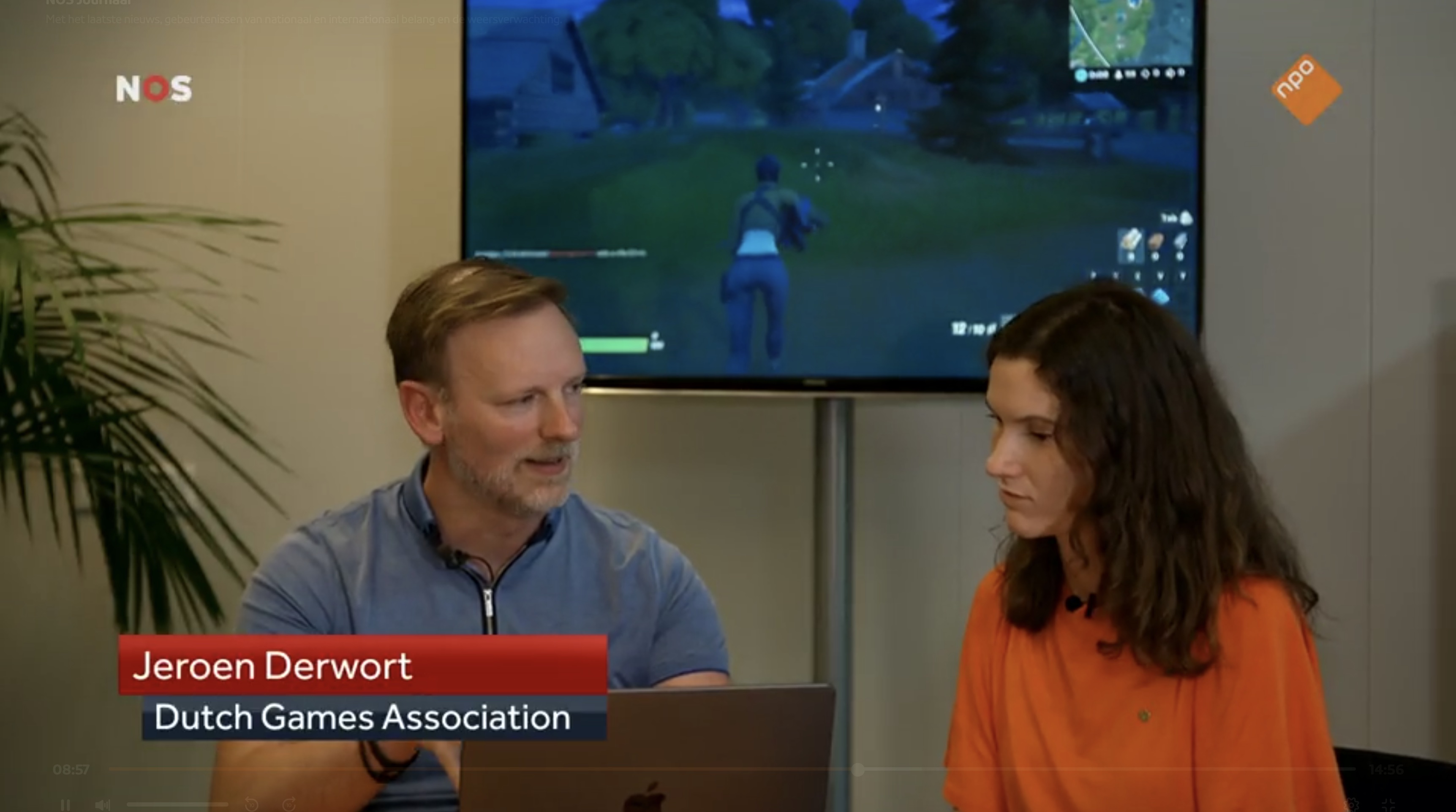 Jeroen Derwort in gesprek met een NOS-journalist, met een game op het scherm achter
hen